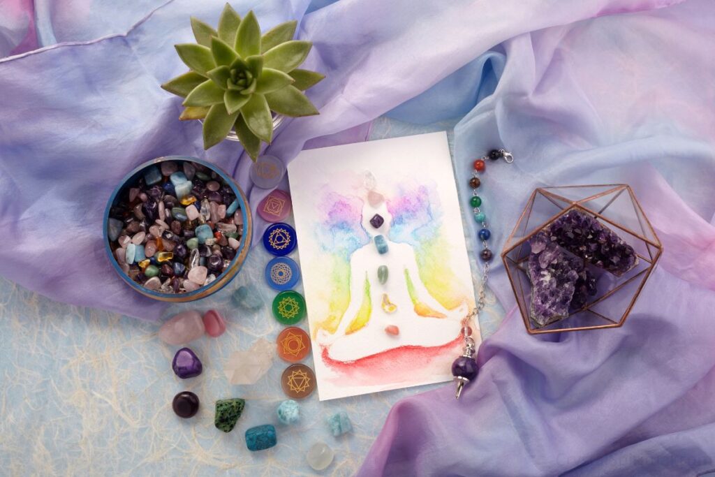 Colorful crystals, gemstones, and a watercolor drawing of chakra points on a purple silk cloth.  Spiritual healing items.