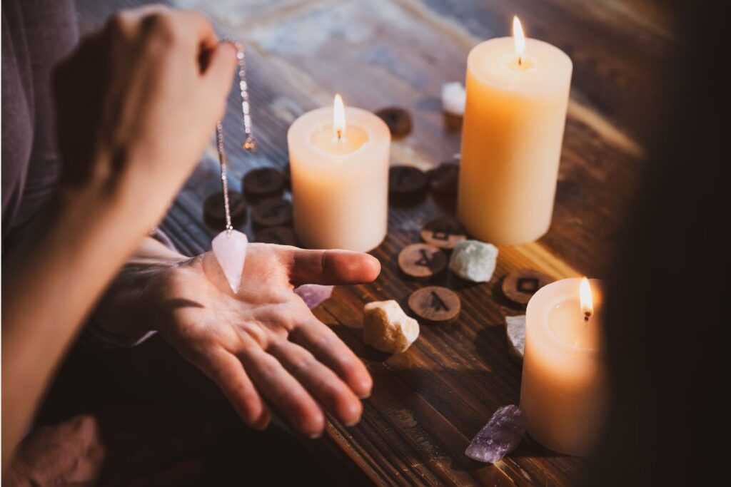 Hand holding pendulum over palm, crystals, and candles.  Psychic reading.