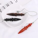 Three gemstone pendulums, brown, black, and red, with pointed tips and decorative bodies, on a white plate.