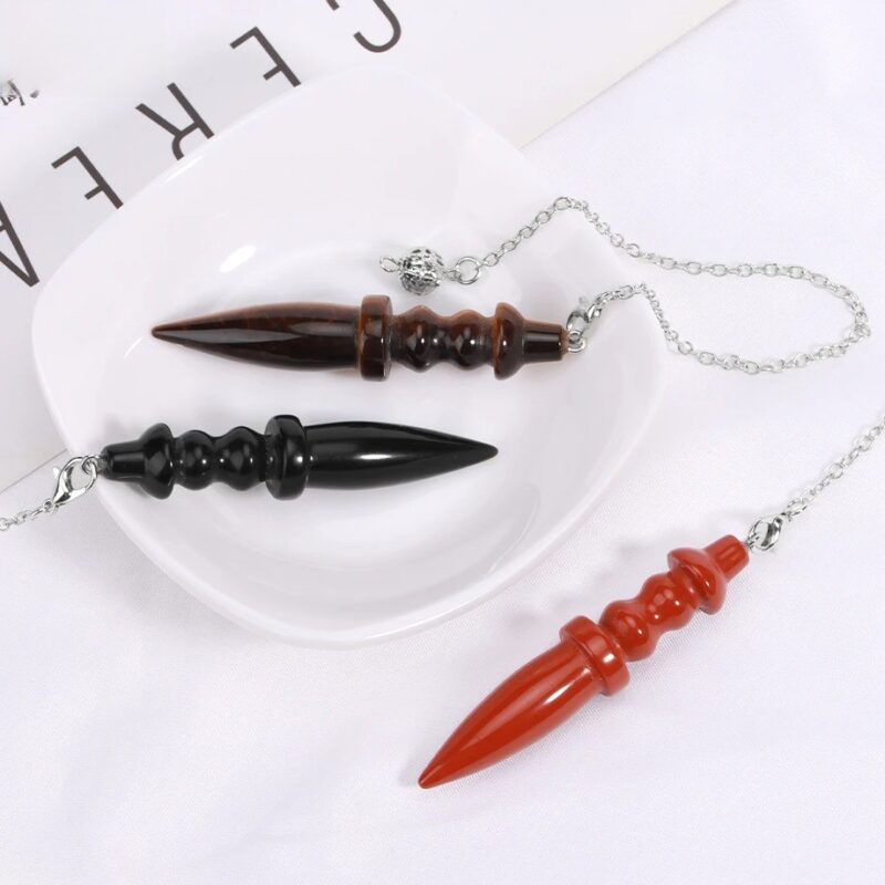Three gemstone pendulums, brown, black, and red, with pointed tips and decorative bodies, on a white plate.