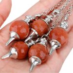 Four  sunstone pendulums, metallic silver bases,  with a hand holding them.