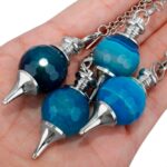 Three teal blue agate pendulums with silver metal tips, held in a hand.  Spiritual, divination tools.