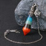 Multi-colored gemstone pendulum with chain and charm, layered crystals.