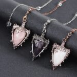 Three crystal pendulums, rose quartz, amethyst, and white, ornate metal frames.