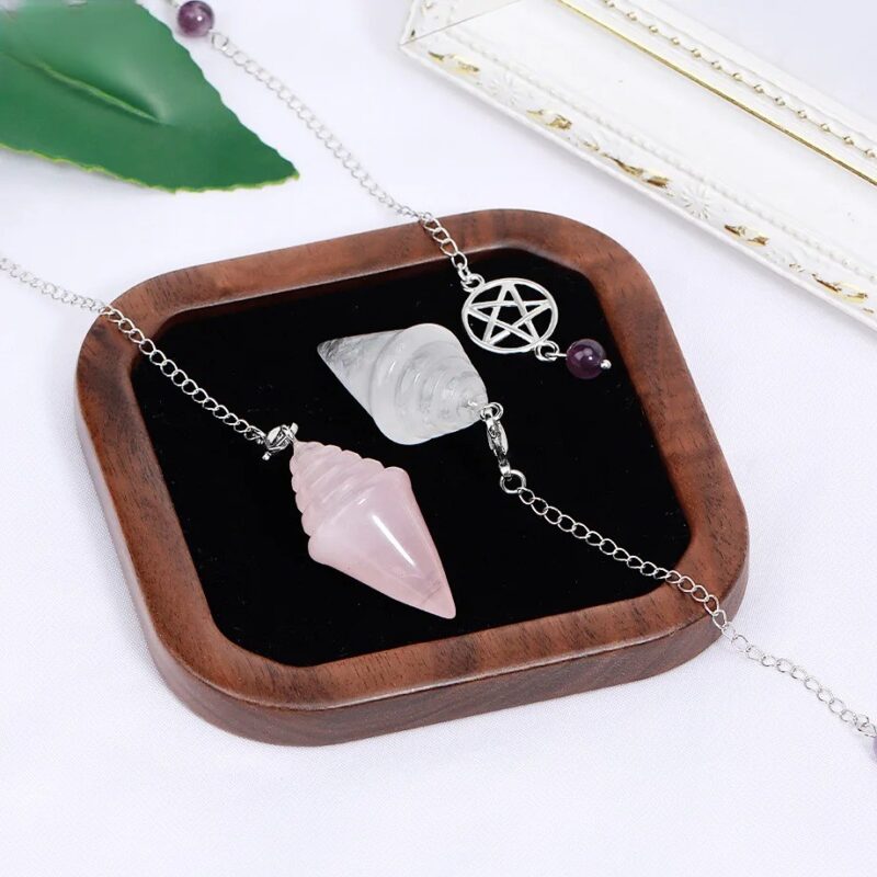 Two crystal pendulums, one rose quartz and one clear quartz, on a wooden tray.  Crystal healing.