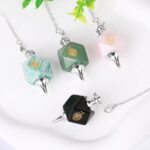 Four crystal pendulums,  green, pink, teal, and black, with a gold spiral symbol,  on chains.  Spiritual, healing.