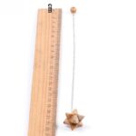Wooden ruler measures a light brown, star-shaped pendulum with a metal chain.