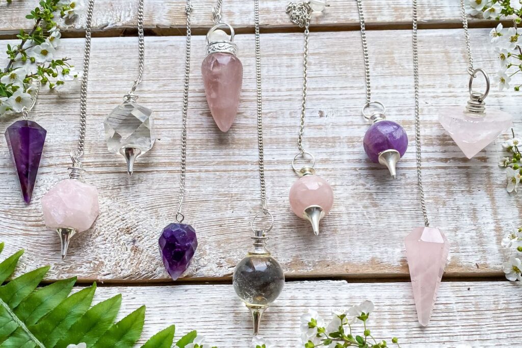 Various crystal pendulums, amethyst, rose quartz, and clear quartz, on a light wooden background.