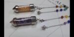 Two crystal pendulums, one with gold/orange crystals, the other with purple crystals, on chains with colored beads.  Spiritual, healing.