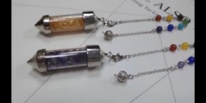 Two crystal pendulums, one with gold/orange crystals, the other with purple crystals, on chains with colored beads.  Spiritual, healing.