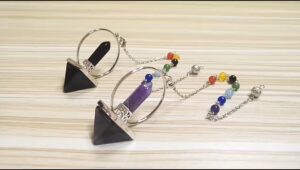 Two crystal pendulums, one with a black and one with a purple stone,  with a rainbow chakra bead chain.