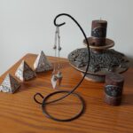 Small pyramids, pendulums, and candle on a wooden surface.