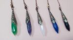 Five gemstone pendulums, various colors (green, amethyst, white, blue, black), with ornate metal caps.