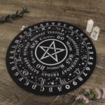 Black Ouija board with white symbols,  star,  days of the week, numbers, and letters.  Wooden table.