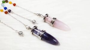 Two crystal pendulums, amethyst and rose quartz, on a white surface.