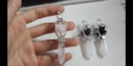 Two crystal pendants, one with rose quartz, the other with amethyst and black stones,  on a light surface.