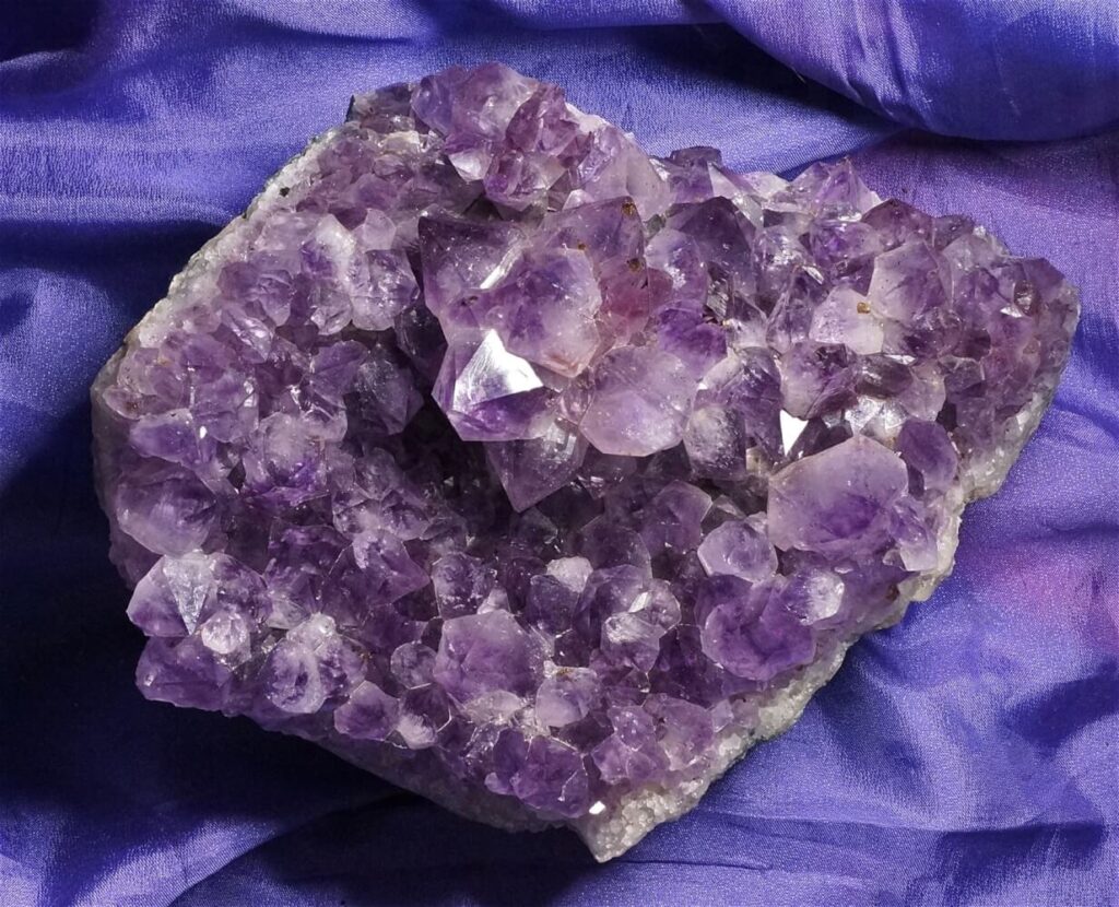Large amethyst cluster on purple fabric.