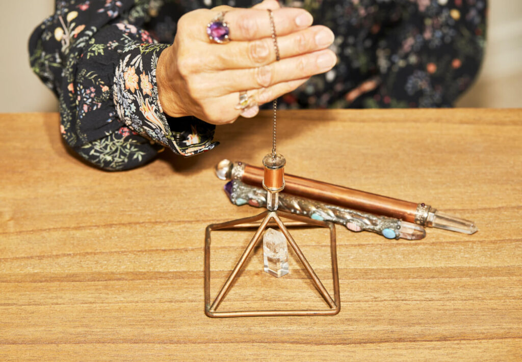 Person holding pendulum over crystal pyramid, divining tools.