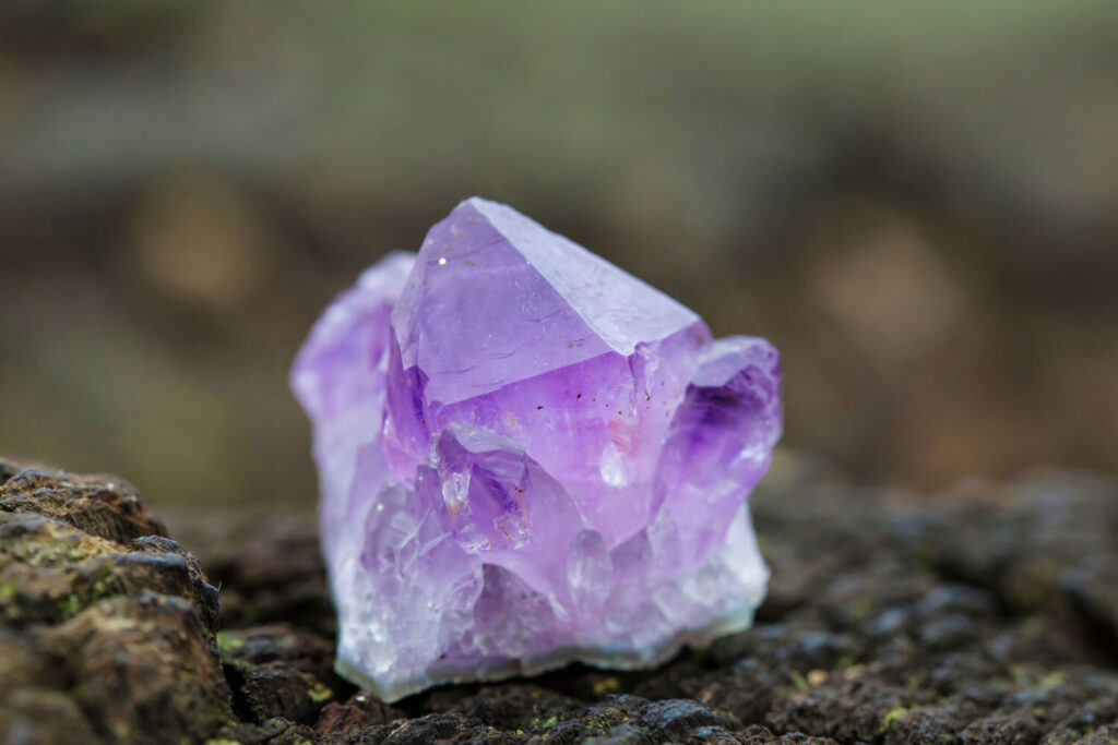 Close-up of a vibrant purple amethyst crystal on a dark, textured surface.