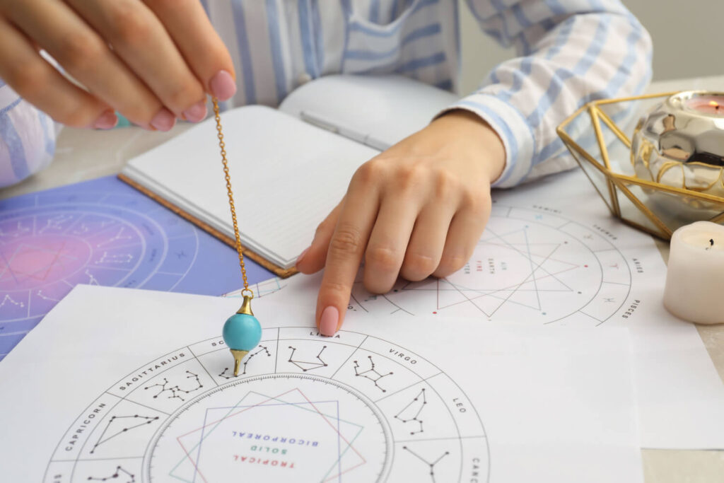 Person using a pendulum for astrology reading, charts, and zodiac signs.