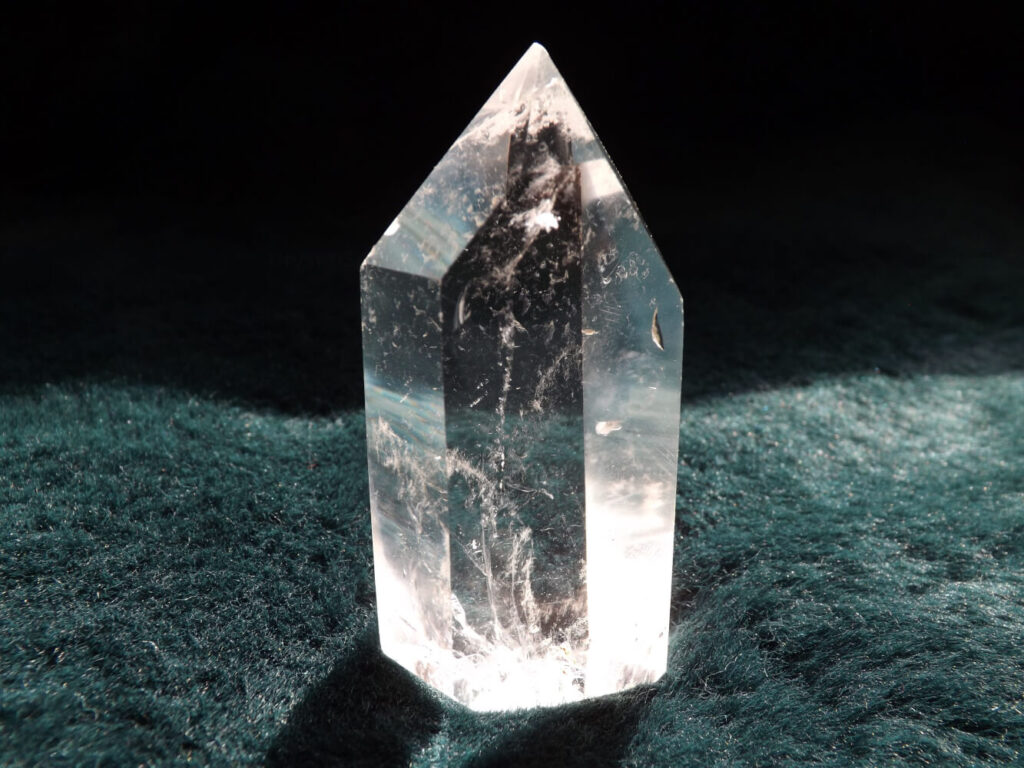 Clear quartz crystal point on dark teal fabric.