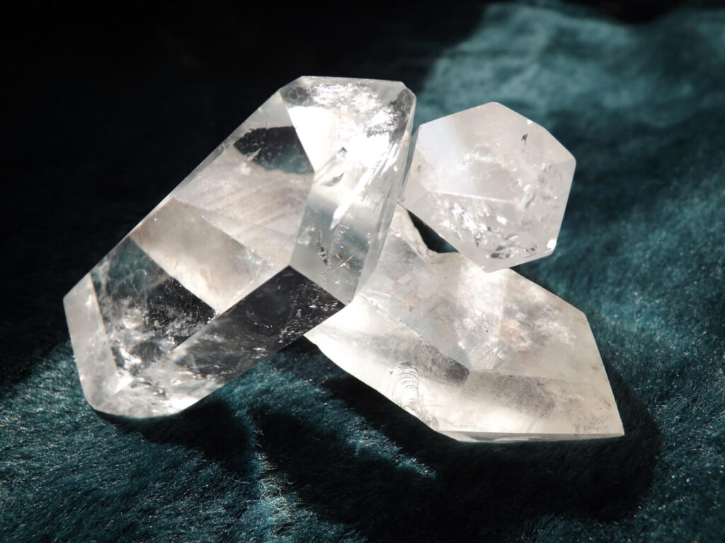 Clear quartz crystals, multiple shapes, on dark teal surface.