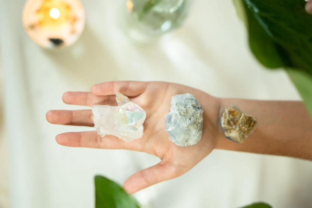 Hand holding three crystals:  clear quartz,  blue calcite, and brown stone.  Wellness, crystals.