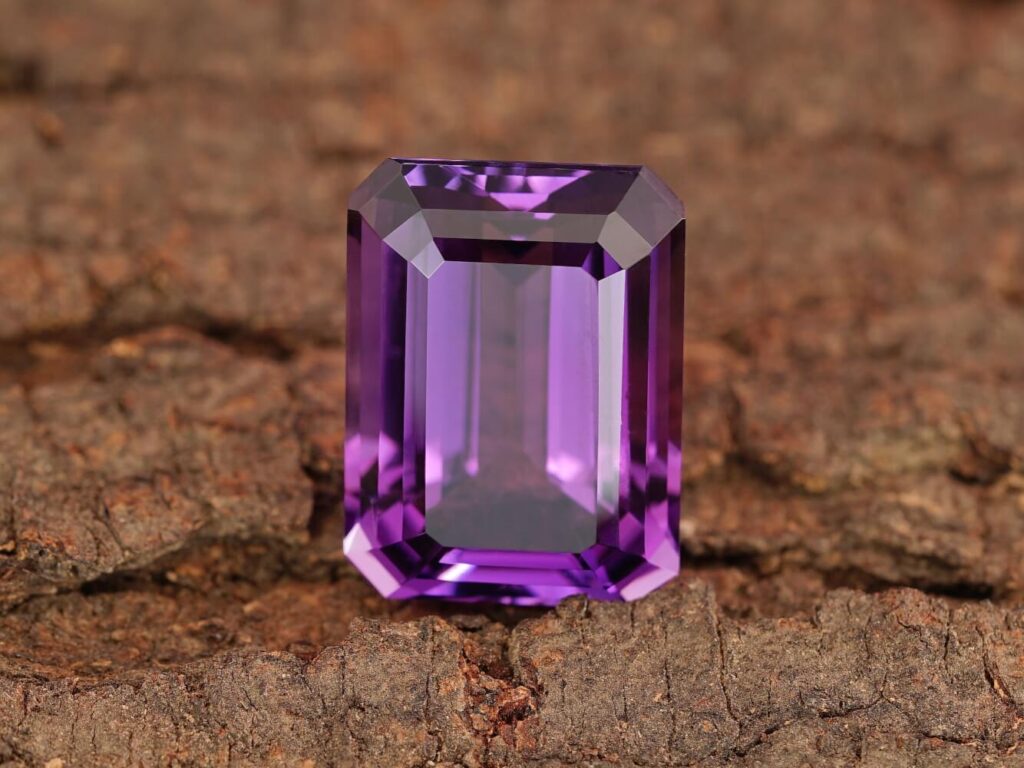 Deep purple emerald-cut amethyst gemstone on wood.