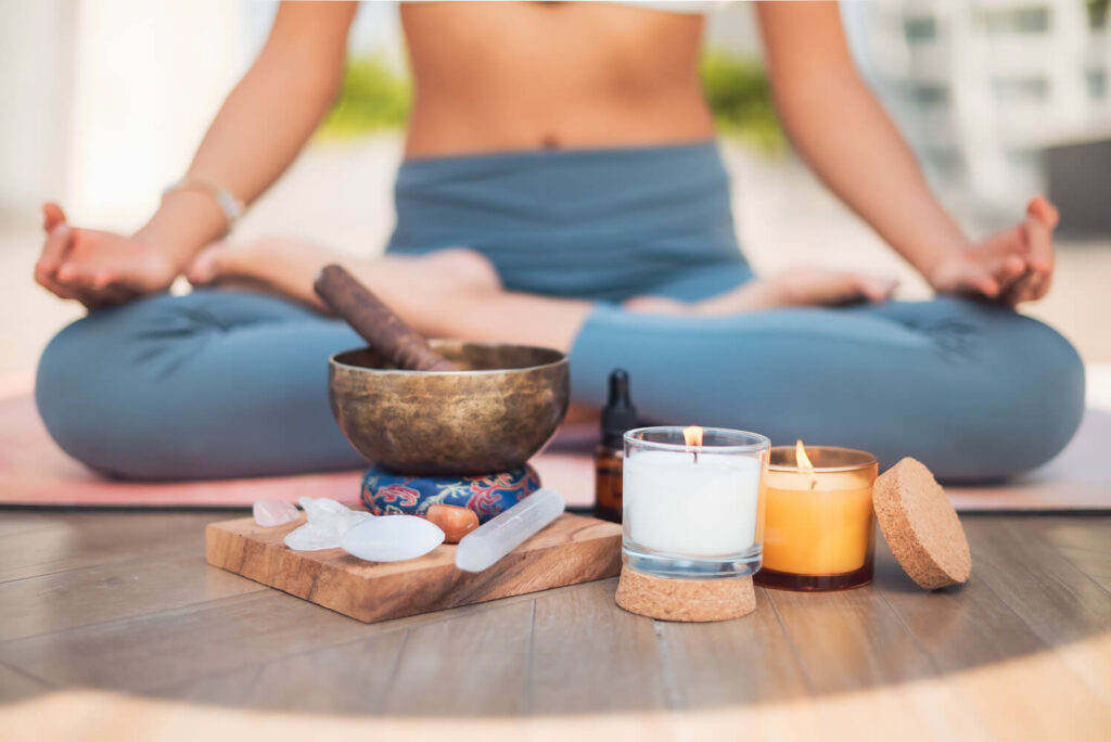 Yoga woman meditating, crystals, singing bowl, and candles for wellness.