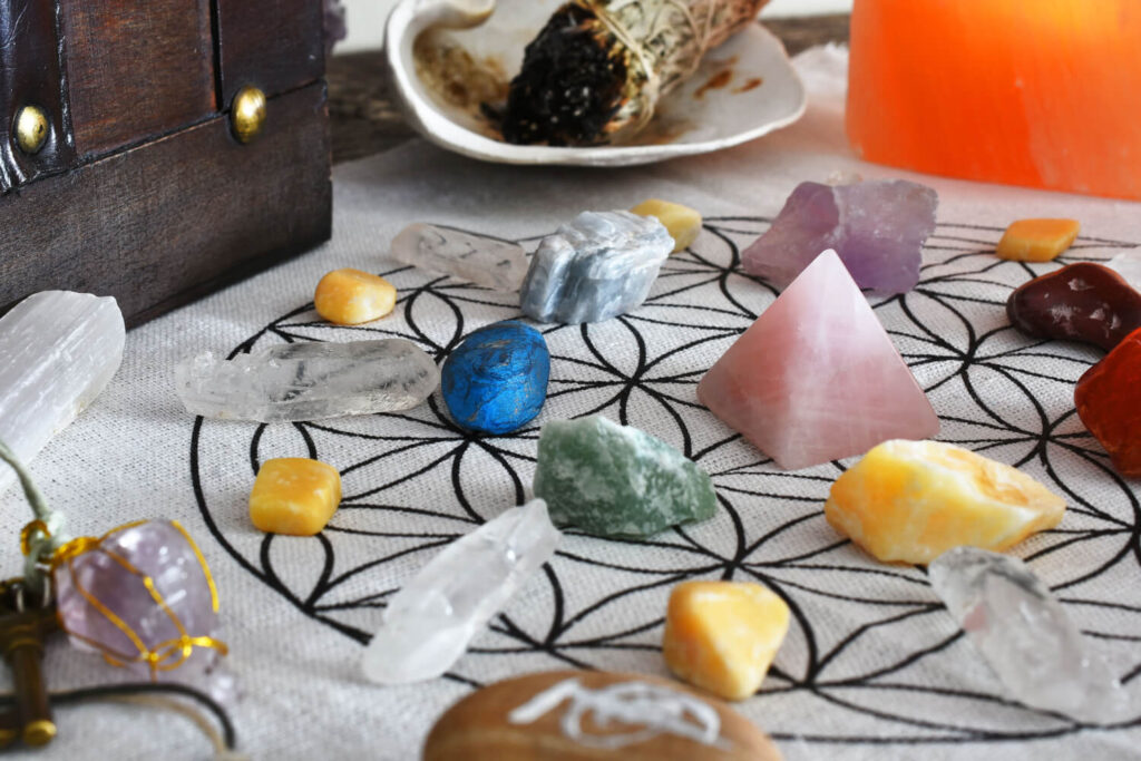 Crystals, stones, and pyramids arranged on a cloth with flower of life pattern. Various colors and shapes.