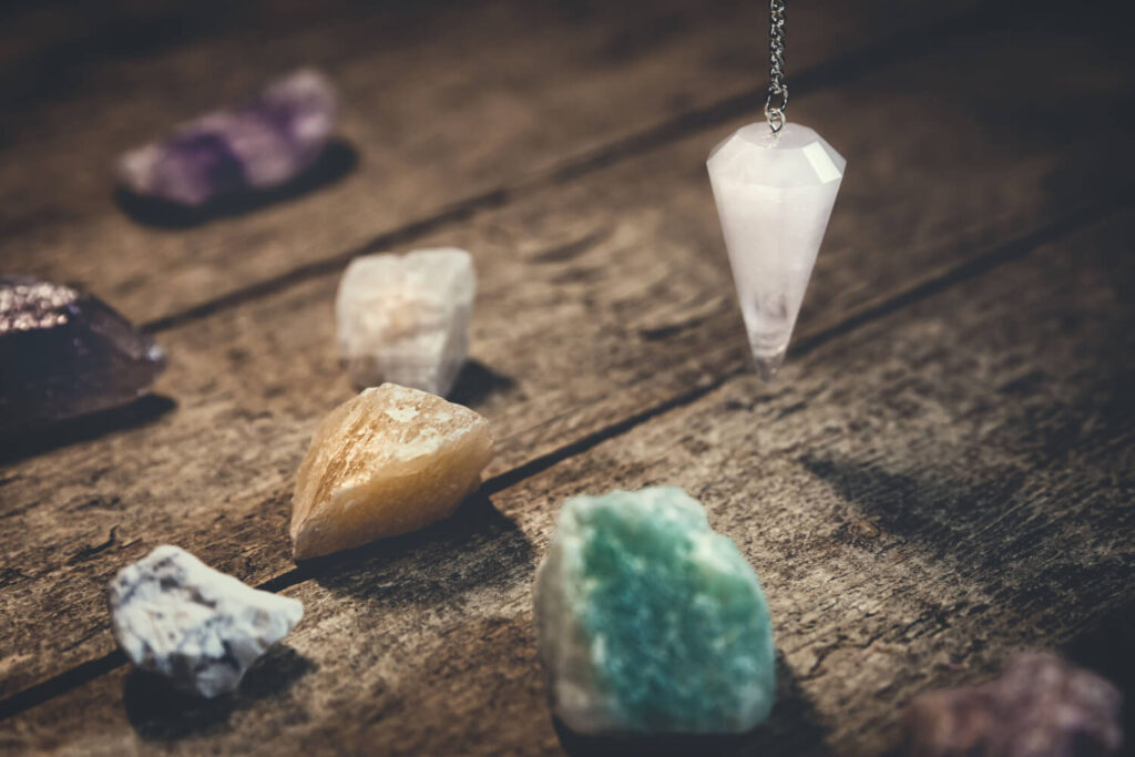 Crystal pendulum, amethyst, citrine, and other stones on rustic wooden table.