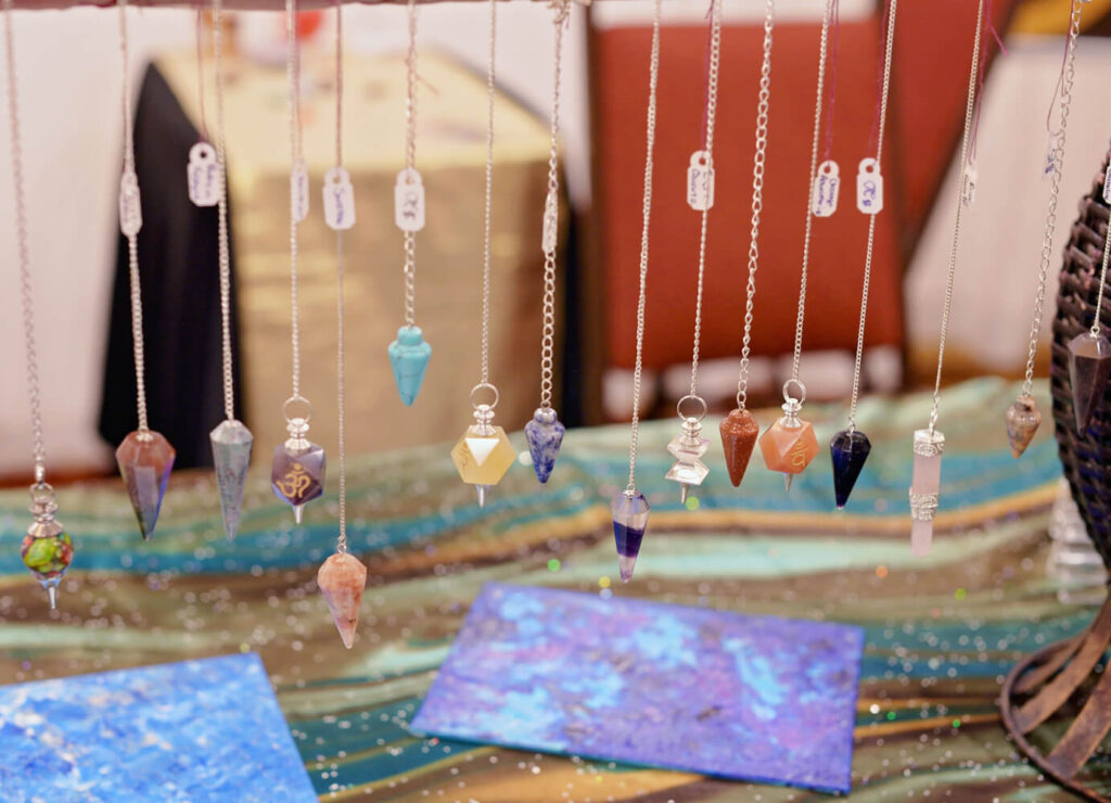 Colorful gemstone pendulums, various shapes and colors, hanging from chains.