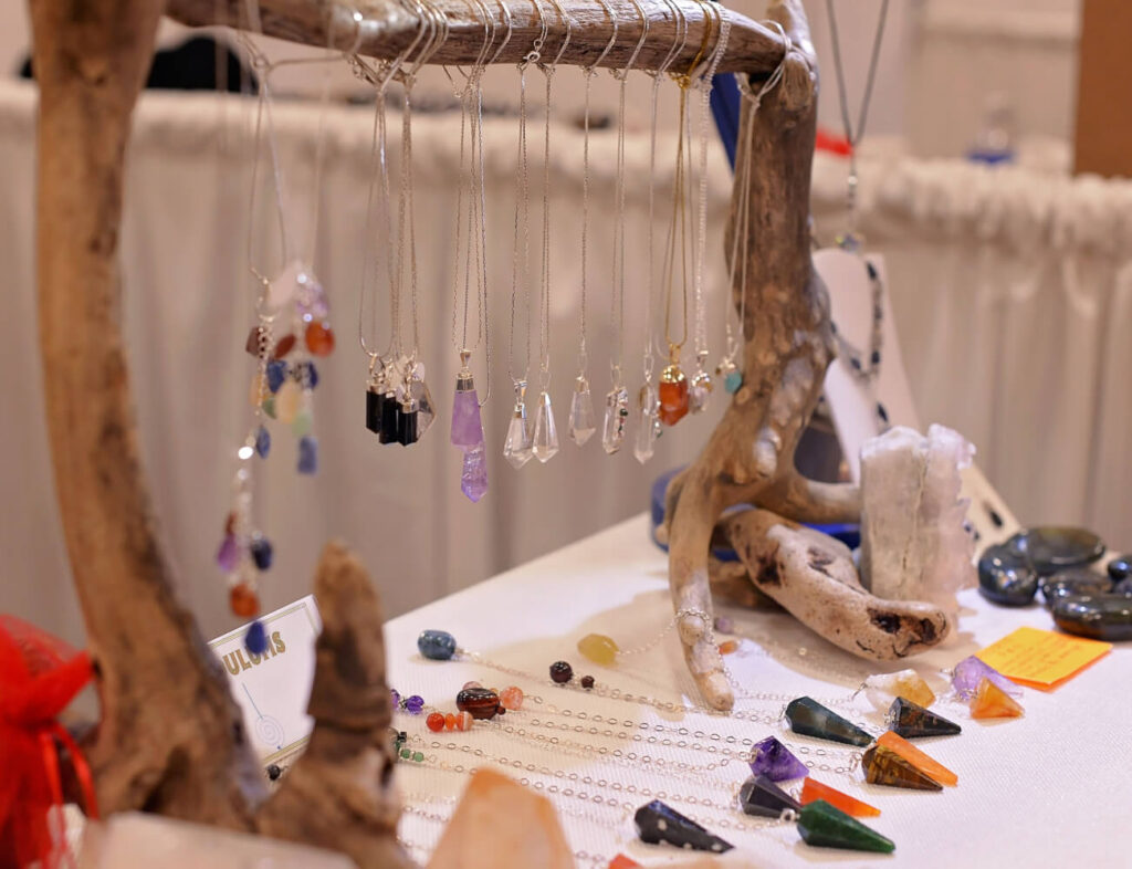 Colorful gemstone necklaces and pendulums displayed on a driftwood stand.
