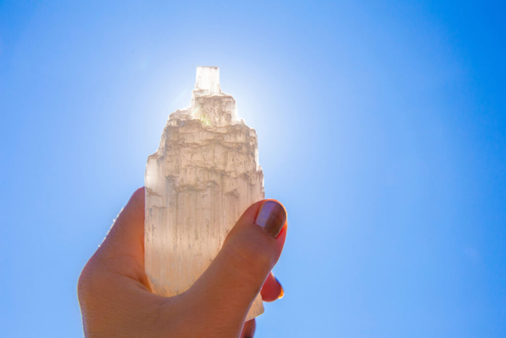 Handheld selenite crystal against a clear blue sky.