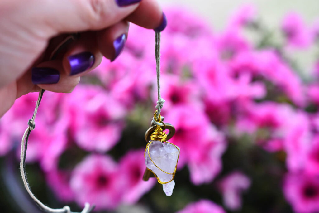 Hand holding a small amethyst key pendant, against a background of pink flowers.