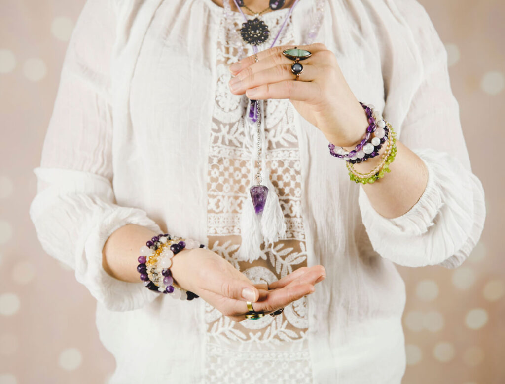 Woman holding amethyst pendulum, wearing bracelets with various gemstones.