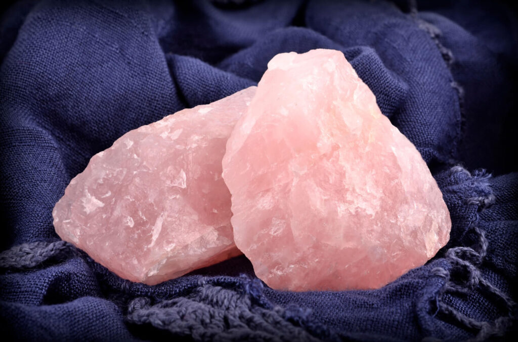 Two raw, pink rose quartz crystals on dark blue fabric.