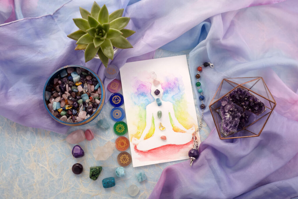 Chakra illustration, crystals, and crystals bowl on soft purple background.