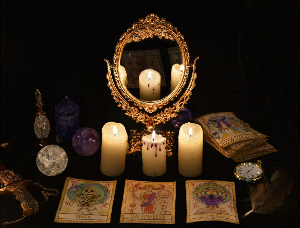 Tarot cards, candles, crystals, ornate mirror, and antique items on a dark background. Occult, divination still life.