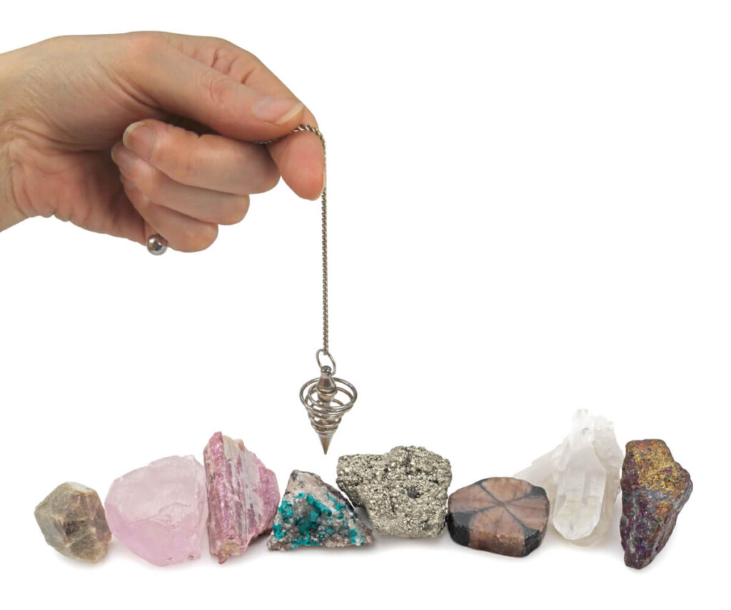 Hand holding pendulum over assorted crystals.