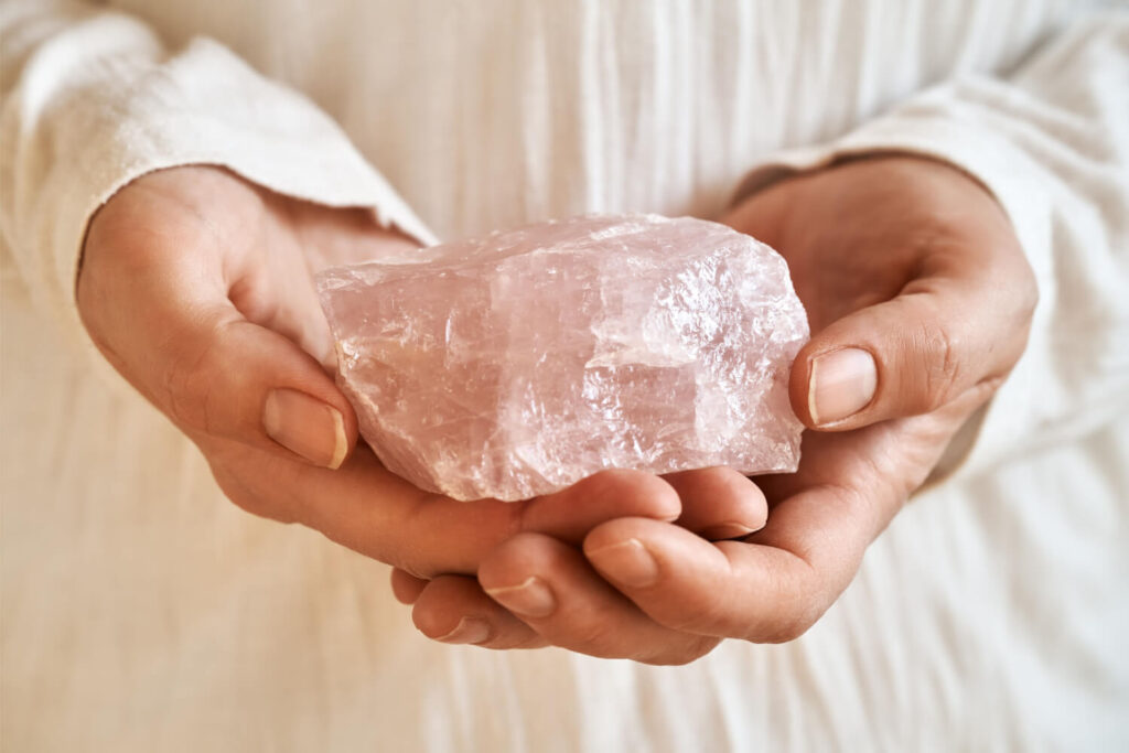 Pink raw quartz crystal held in hands.
