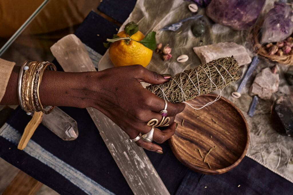 Person holding sage smudge stick, crystals, and jewelry.  Spiritual practice.
