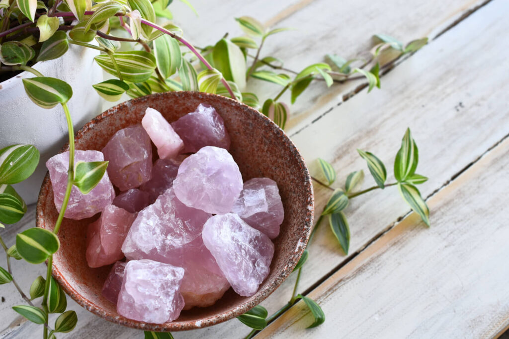 Pink raw quartz crystals in a rustic bowl, surrounded by greenery.