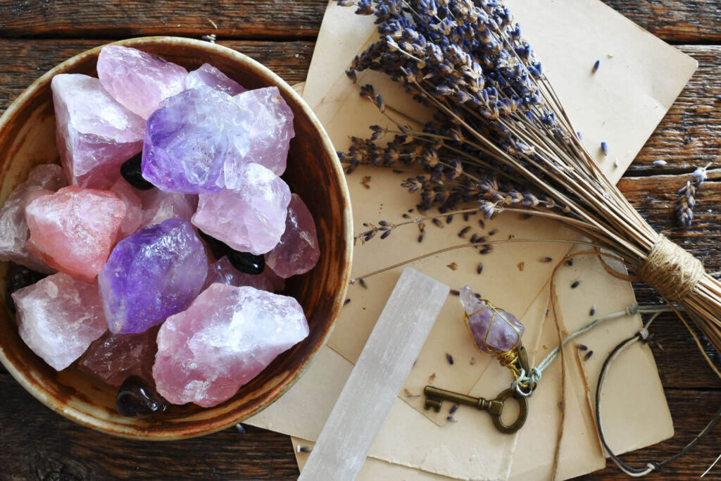 Pink, purple, and clear crystals in a bowl, dried lavender, a selenite wand, and an antique key.  Spiritual, healing, and crystals.