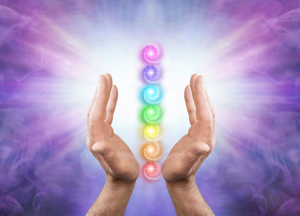 Hands holding chakra energy centers, colorful rainbow energy.