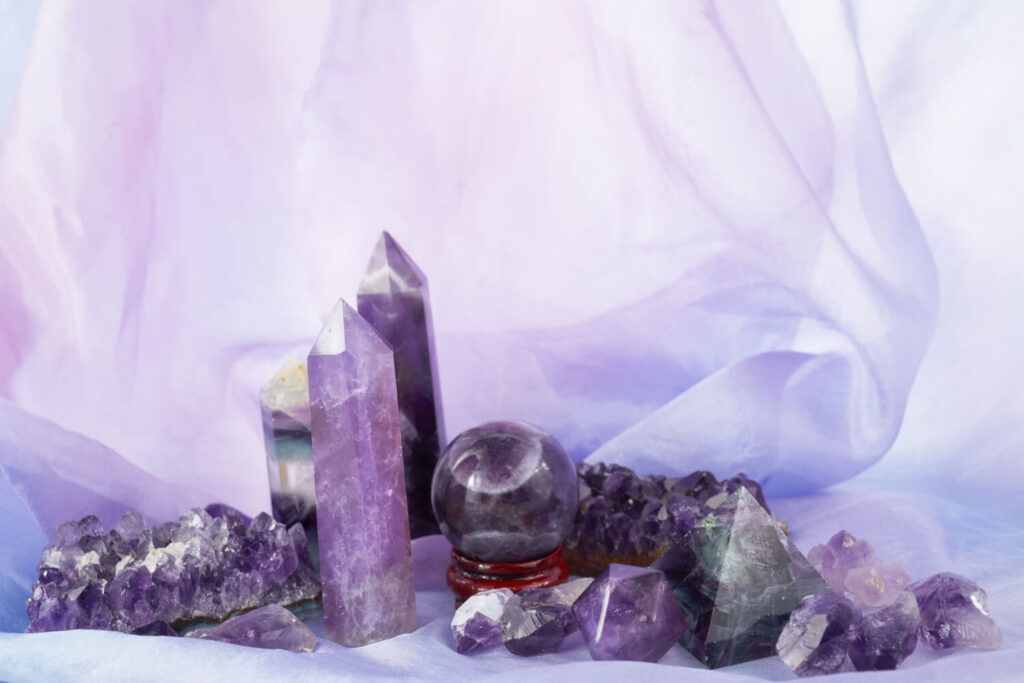 Purple amethyst crystals and other stones on a pastel purple fabric. Healing crystals.