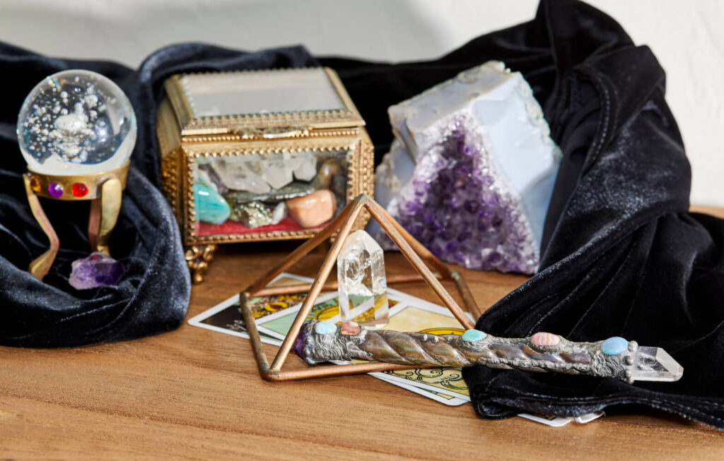 Crystal divination spread with gemstones, ornamental box, pyramid, wand, and tarot cards. Black velvet cloth.