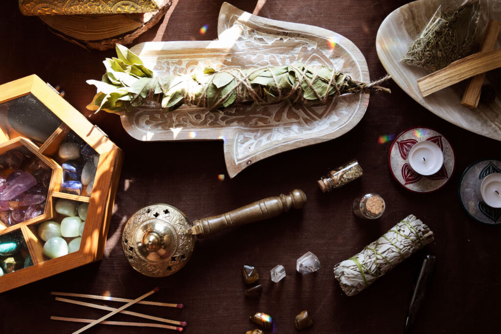 Overhead view of crystals, sage smudge sticks, candles, and other spiritual items on a dark brown surface.