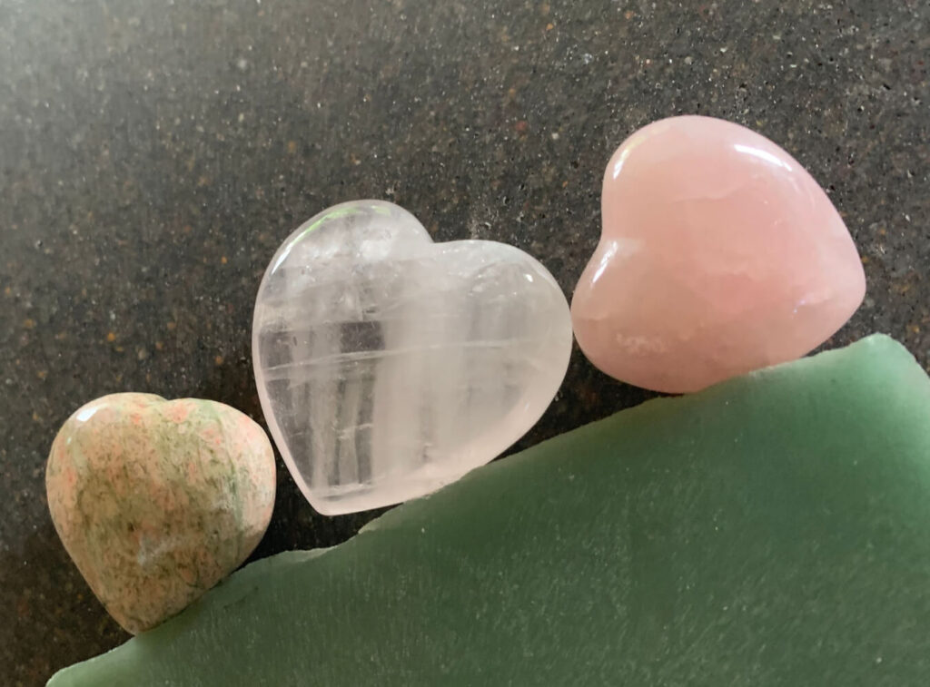 Three heart-shaped crystals:  rose quartz, clear quartz, and a mottled peach/green stone.