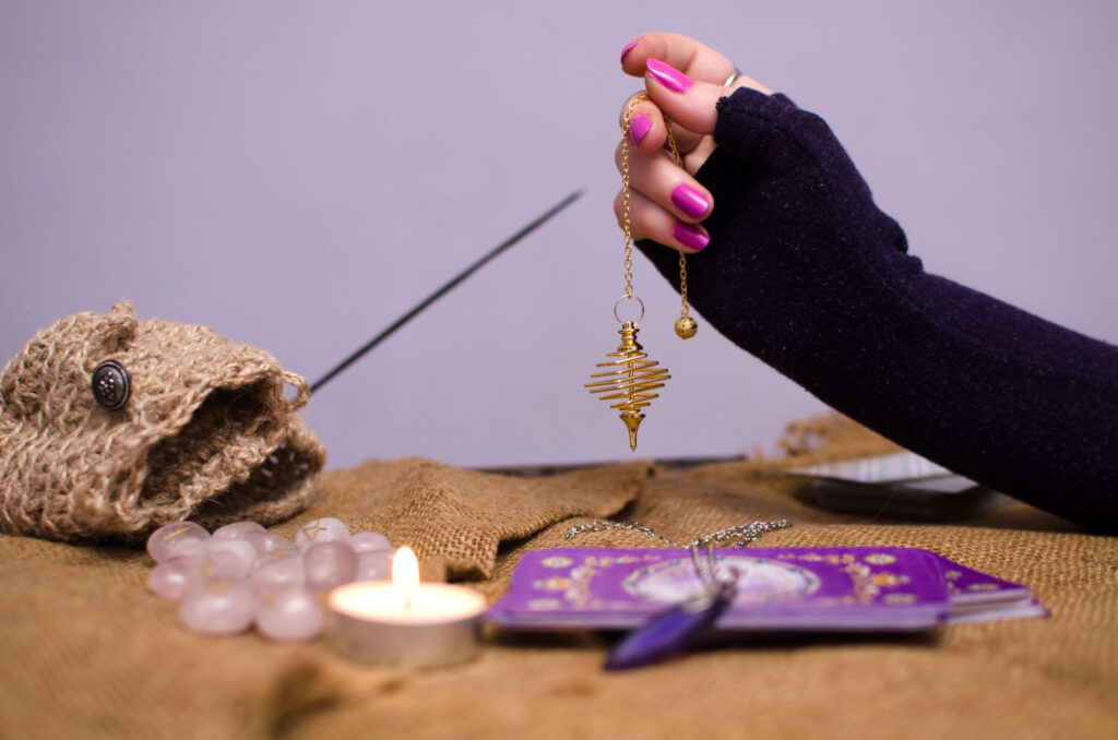 Tarot cards, pendulum, crystals, and candle on burlap cloth. Spiritual practices.